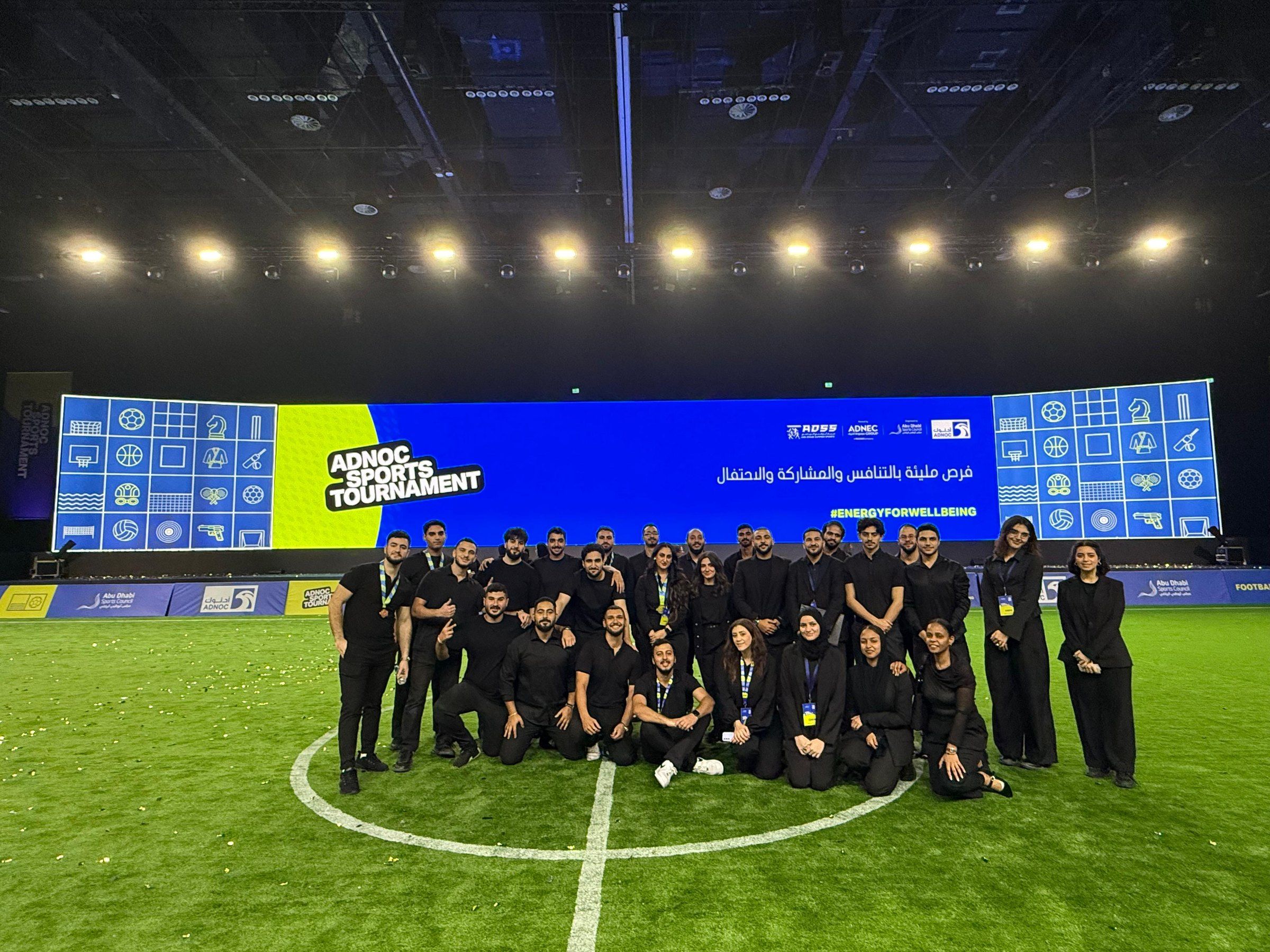 One Team crew in black uniforms lined up on the floodlit pitch at the ADNOC Sports Tournament