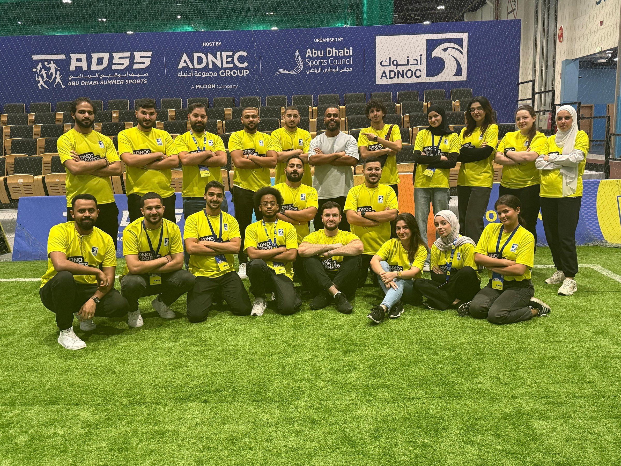 One Team staff in yellow shirts posing on the indoor pitch at Abu Dhabi Summer Sports
