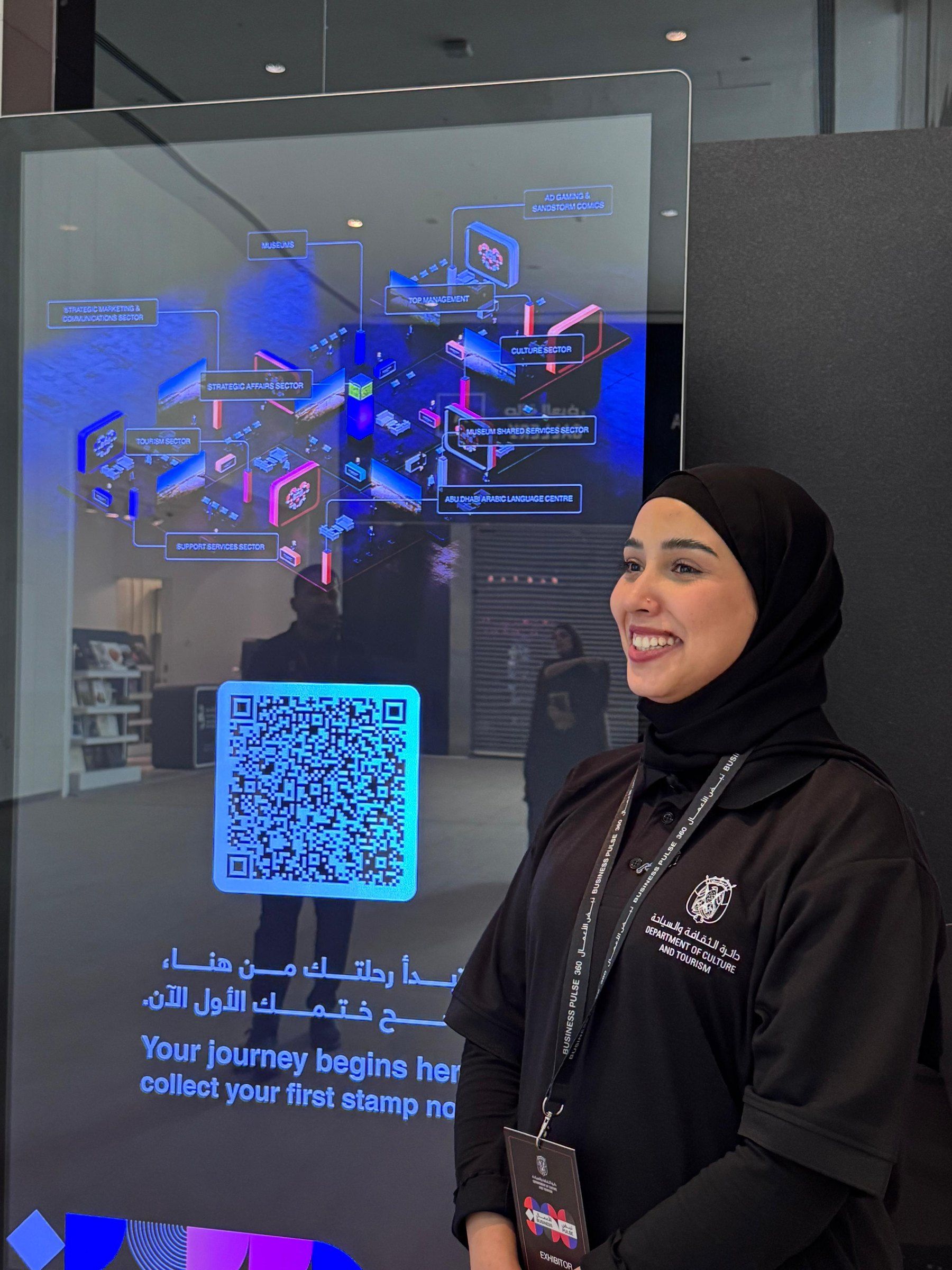 A host in uniform beside a glowing interactive screen at an immersive experience