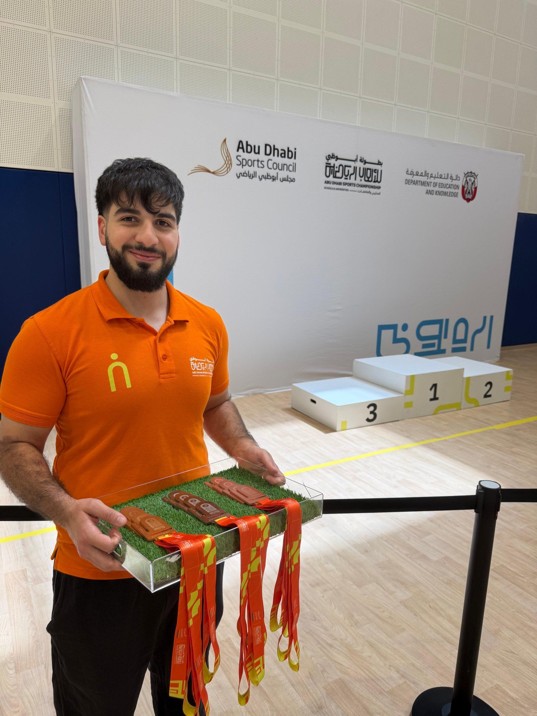 A host holding a tray of medals beside the winners podium