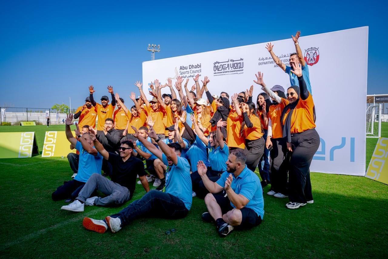 One Team staff in orange shirts cheering in front of the championship backdrop