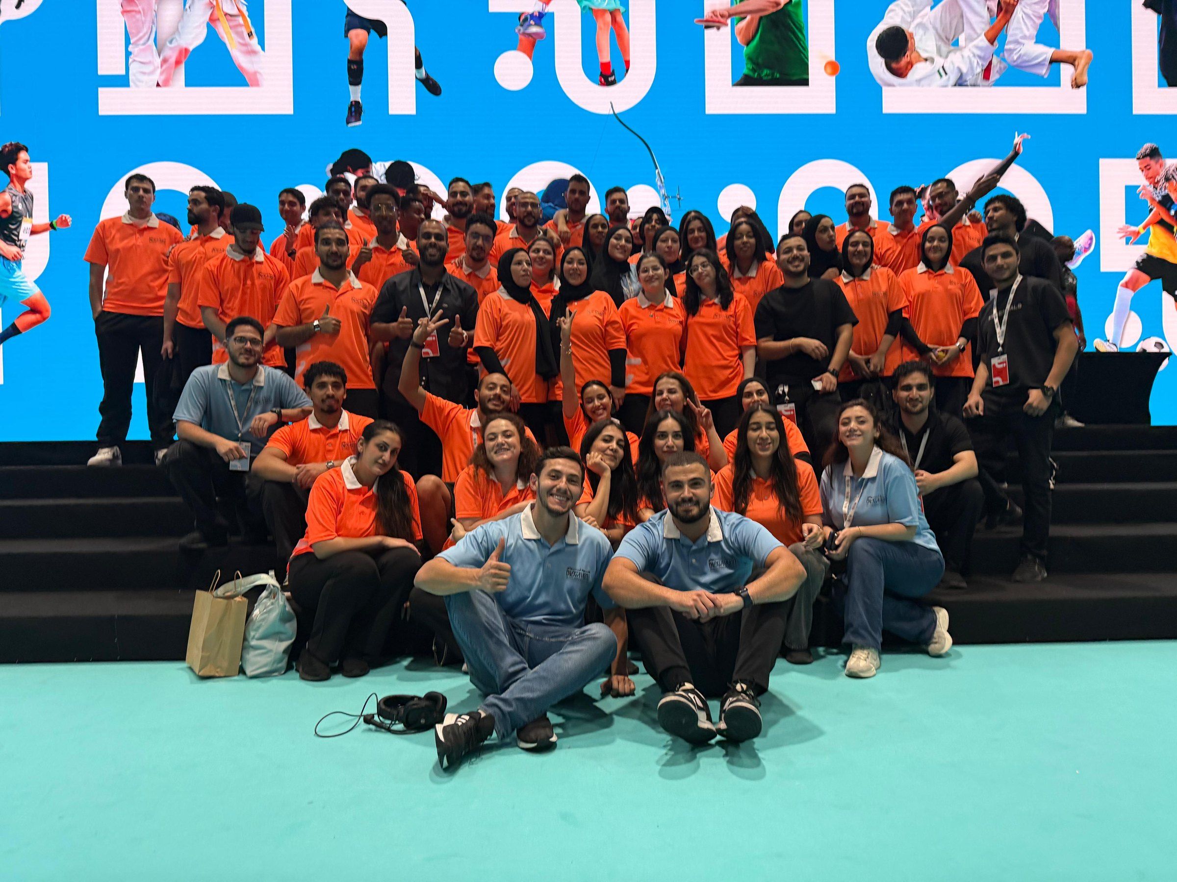 The orange-shirted team posing on stage steps